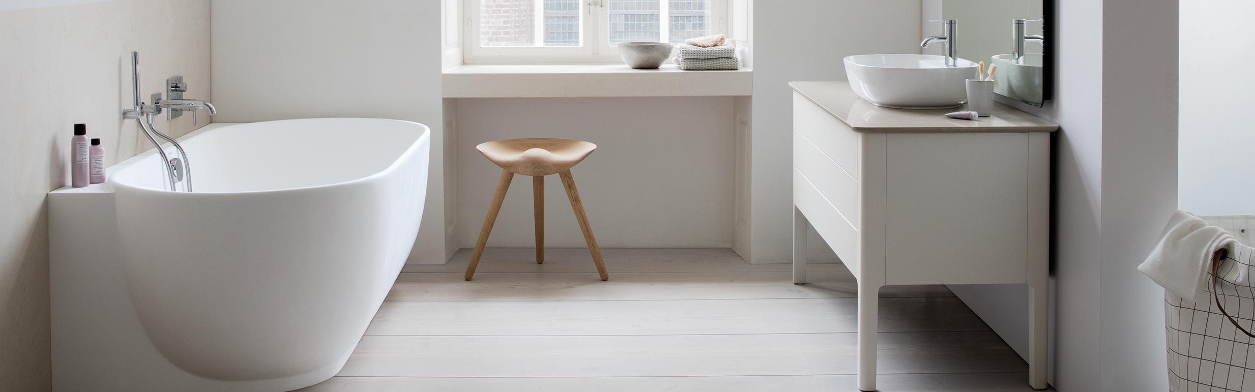 Ein minimalistisches Badezimmer mit einer freistehenden weißen Badewanne und einer modernen Armatur an der Wand. 