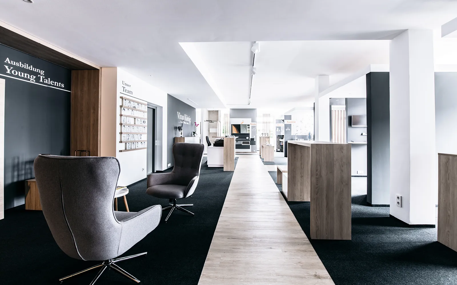 Ein geräumiger und moderner Showroom mit grauen Loungesesseln und Holzelementen in einem hellen, minimalistischen Design. 