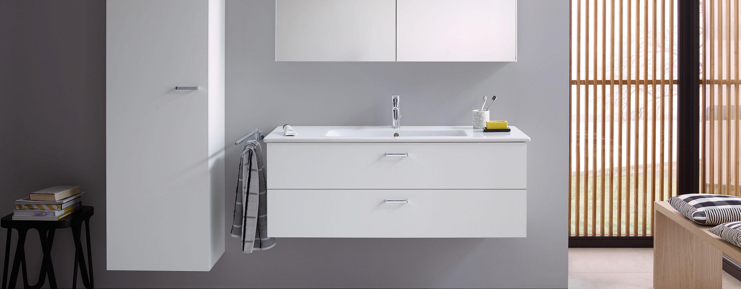 Helles Badezimmer mit der Badmöbelserie XBase von Duravit, bestehend aus einem weißen Waschtisch, Hochschrank und Spiegel.