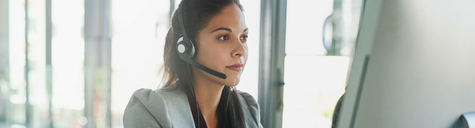 Frau sitzt mit Headset vor dem PC