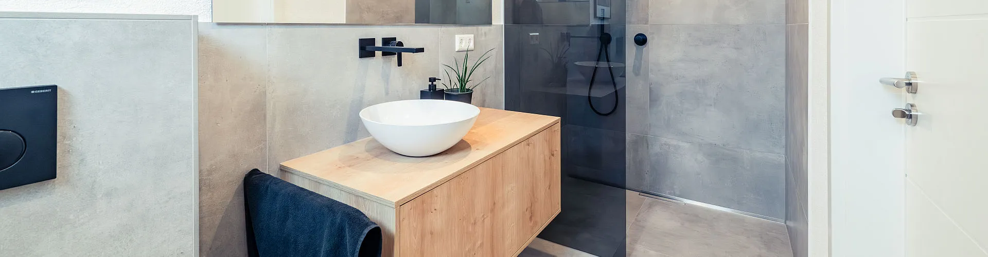 Stilvolles Gästebad mit minimalistischem Waschtisch aus Holz, weißem Aufsatzbecken und mattschwarzer Wandarmatur.