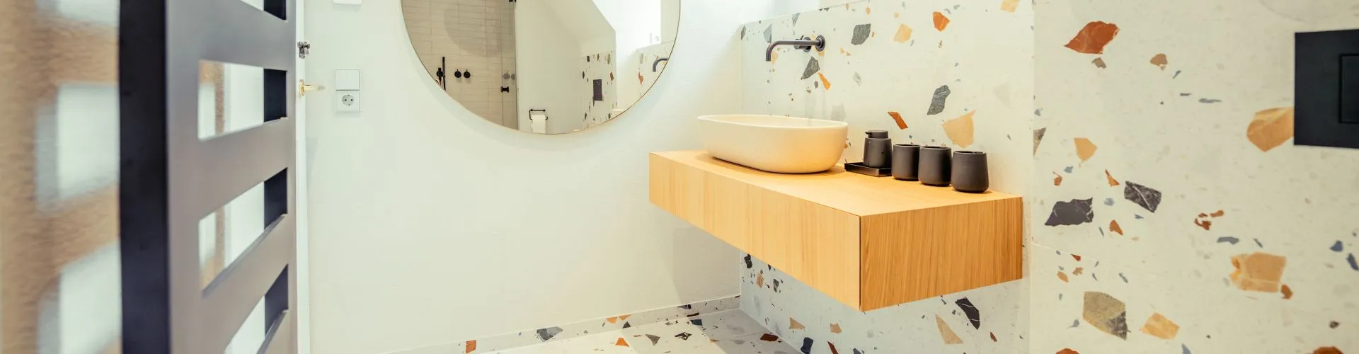 Helles Badezimmer mit minimalistischer Ausstattung, schwebendem Waschtischunterschrank aus Holz und Terrazzo-Fliesen.