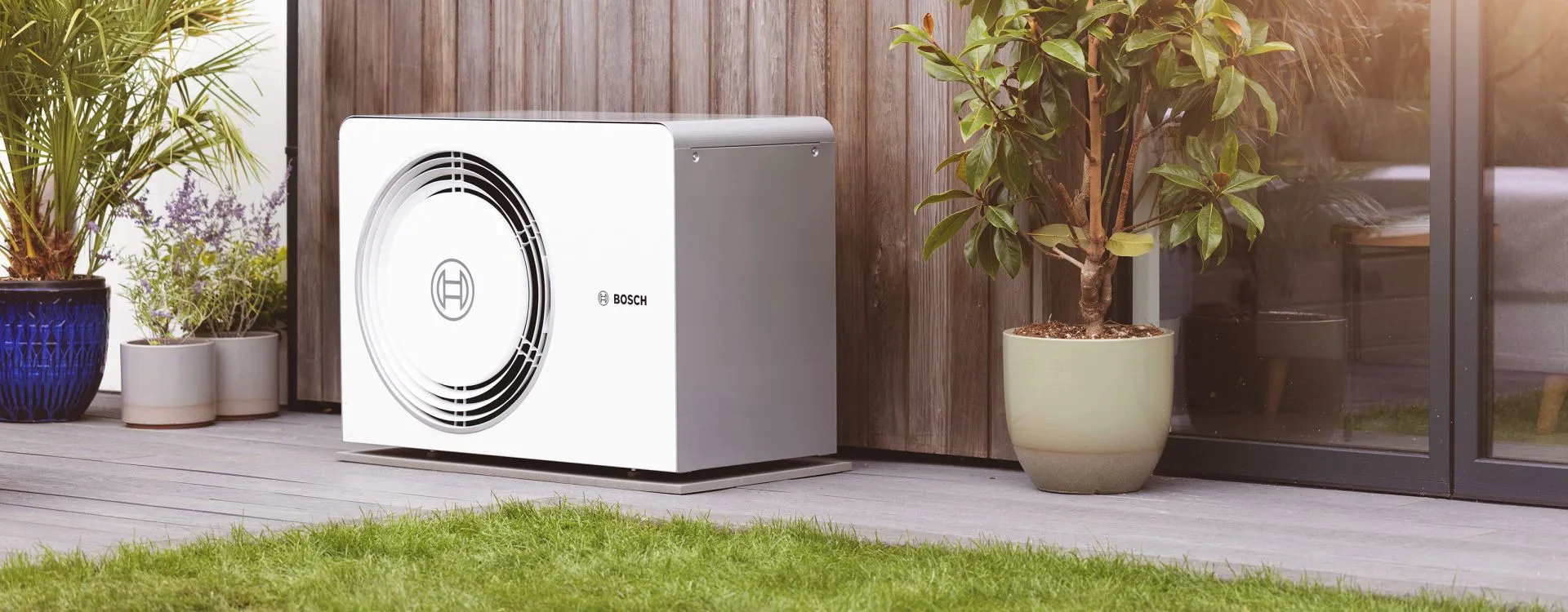 Eine weiße Wärmepumpe von Bosch steht vor einer mit Holz verkleideten Hauswand.