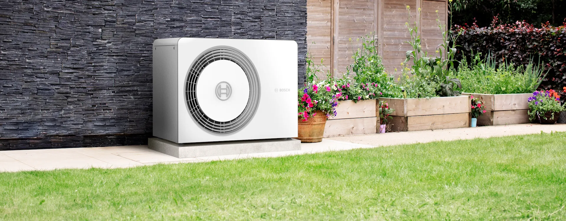 Die Waermepumpe der Serie Compress 5800 von Bosch vor einer dunklen Hauswand im Garten.