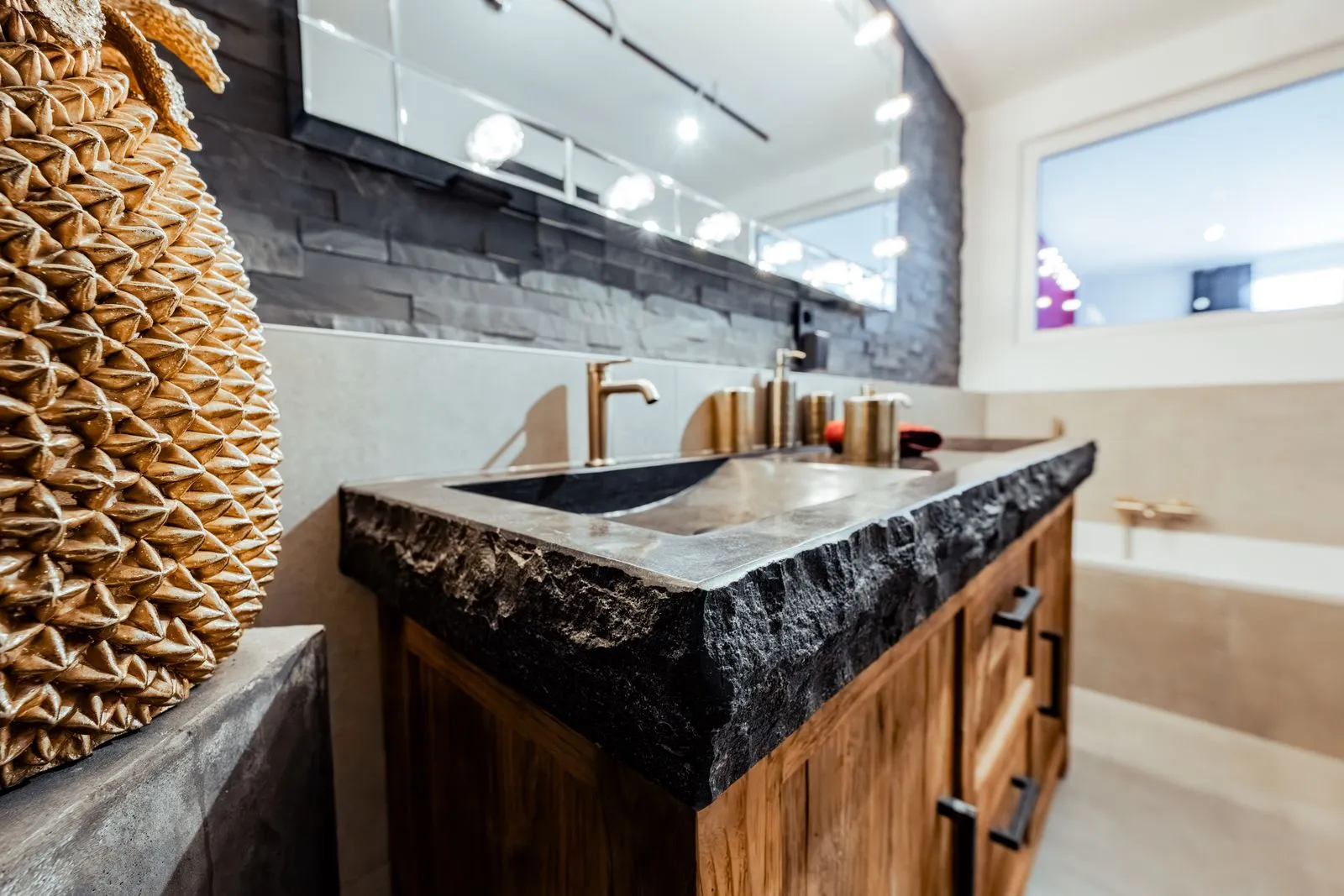 Detailansicht eines Holzwaschtischs mit massiver Natursteinplatte und Armatur in Goldoptik.