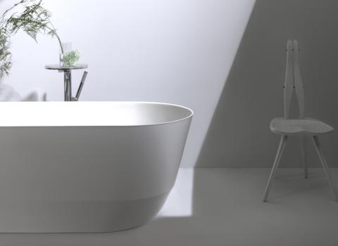 Ein minimalistisches Badezimmer mit einer freistehenden weißen Badewanne vor einer hellgrauen Wand.