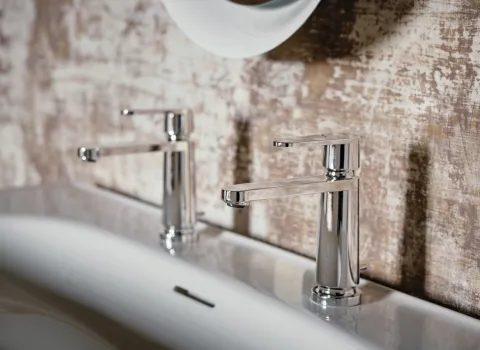 Zwei verchromte Wasserhähne mit flachem Auslauf sind nebeneinander auf einem Doppelwaschbecken montiert. 