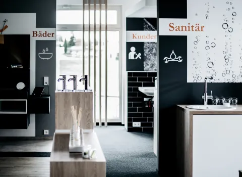 Ein moderner Showroom zeigt verschiedene Bereiche für Bad- und Sanitärinstallationen mit Schildern wie "Bäder", "Kundendienst" und "Sanitär".