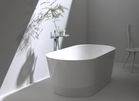 Eine freistehende, rechteckige Badewanne steht in einem minimalistischen Badezimmer, das von weichem Licht erhellt wird. 