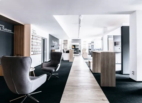 Ein geräumiger und moderner Showroom mit grauen Loungesesseln und Holzelementen in einem hellen, minimalistischen Design. 