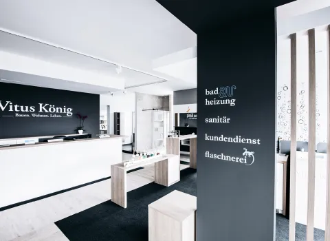 Ein modernes und helles Geschäftslokal zeigt eine Empfangstheke mit der Aufschrift „Vitus König – Bauen. Wohnen. Leben.“ auf einer schwarzen Wand im Hintergrund.