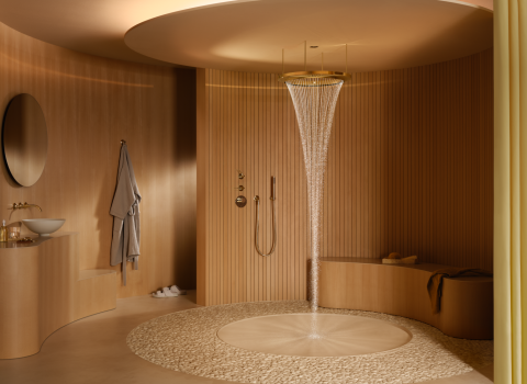 Ein luxuriöses Badezimmer mit einer goldenen, freihängenden Regendusche, aus der ein gleichmäßiger Wasserstrahl auf einen runden Kieselboden fällt. 