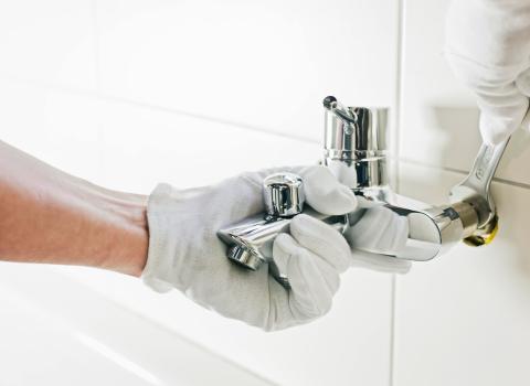 Ein Installateur mit weißen Handschuhen montiert einen glänzenden Wasserhahn an der Badezimmerwand. 