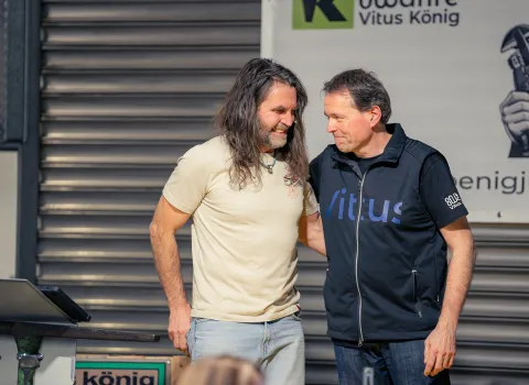 Bei einer Veranstaltung stehen zwei Männer einander zugewandt auf einer Bühne oder einem Podest.