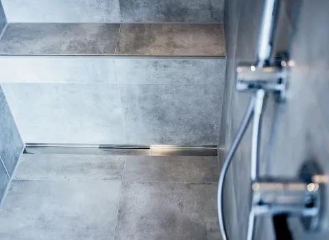 Nahaufnahme Dusche mit Ablaufrinne in Chrom und gemauerter Sitzbank.