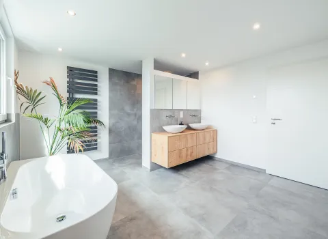 Luxuriöses Bad mit viel Platz, bestehend aus eleganter Badewanne, schwebendem Holzwaschtisch und stilvollen Spiegeln.