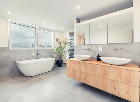 Ein großzügiges Badezimmer mit freistehender Badewanne vor großen Fenstern, die viel Tageslicht hereinlassen.