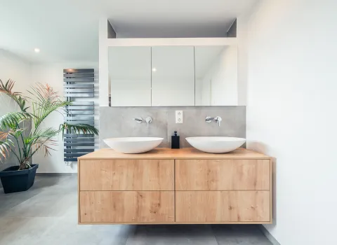 Ein elegantes Designerbad mit Doppelwaschplatz aus Holz und zwei weißen Aufsatzbecken. Über dem Waschtisch befindet sich ein großer Spiegelschrank, der für Stauraum und Helligkeit sorgt.