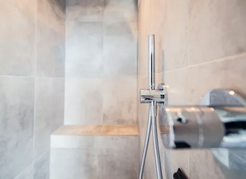 Detailaufnahme des gefliesten Innenbereichs der Walk-in-Dusche mit glänzender Chromarmatur gemauerter Sitzbank.