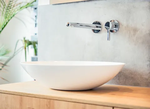 Detailaufnahme eines modernen Aufsatzwaschbeckens aus weißer Keramik, das auf einem Holzwaschtisch platziert ist.