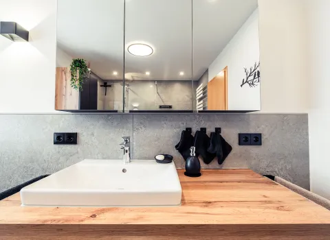 Ein moderner Waschtisch mit rechteckigem Aufsatzwaschbecken steht auf einer eleganten Holzplatte vor einem großen Spiegelschrank.