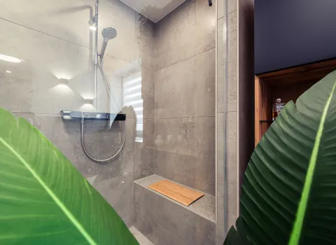 Eine moderne begehbare Dusche mit großformatigen Fliesen in Betonoptik und integrierter Sitzbank aus Stein.