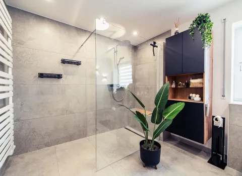 Eine großzügige Walk-In-Dusche mit bodengleichem Einstieg, Glasabtrennung und großen Fliesen in Betonoptik.