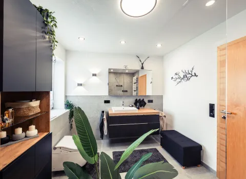 Ein elegantes Badezimmer mit wandhängendem WC, großzügigem Waschplatz und dekorativen Elementen wie Pflanzen, Kerzen und Holzdetails.