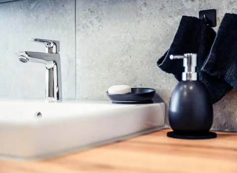 Detailaufnahme eines modernen Waschtischs mit glänzender Chromarmatur auf einem weißen Keramikbecken.