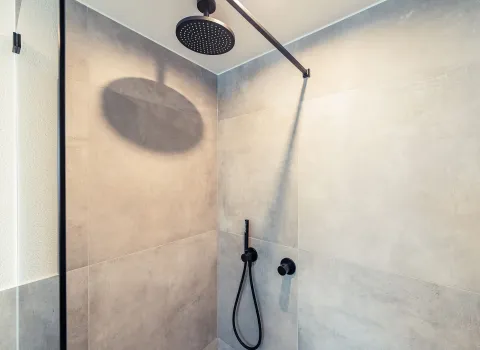 Eine große Regenbrause ist in einer schlichten, modernen Dusche mit großformatigen Betonoptik-Fliesen installiert..