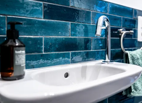 Gäste-Waschtisch mit seitlich angebrachter Armatur vor einer Wand aus blauen Fliesen im urbanen Stil.
