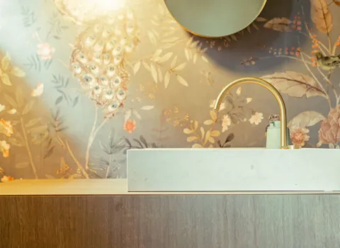 Zentral im Bild steht ein rechteckiges Waschbecken mit goldfarbener Armatur, das sich harmonisch in einen Unterschrank mit Holzoptik einfügt.