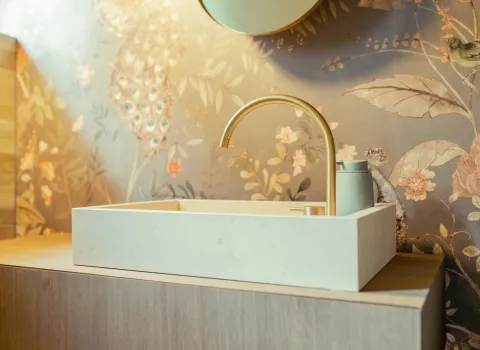 Ein eckiges Aufsatzwaschbecken in Cremeweiß steht auf einem Holzunterschrank, ergänzt durch eine elegante, goldfarbene Armatur.