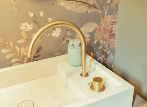 Eine elegante, goldfarbene Armatur mit gebogenem Auslauf ist in ein eckiges Aufsatzbecken integriert.