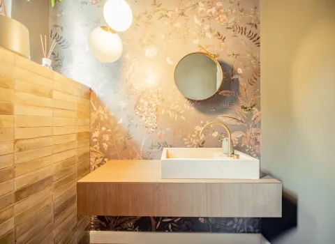 Premium-Holzwaschtisch mit rundem Spiegel und Aufsatzbecken vor einer mit Blumen verzierten Motivtapete.