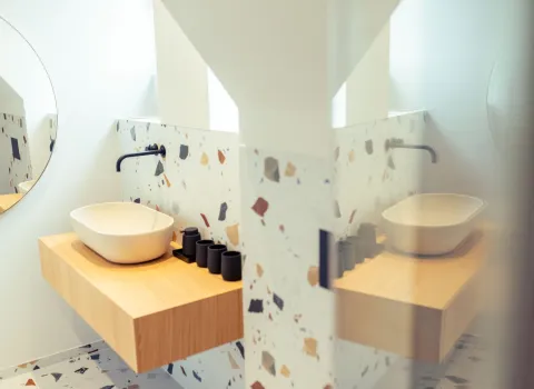 Die Spiegelung im Badezimmer erzeugt einen spannenden Effekt aus Symmetrie und Tiefe. Das Aufsatzbecken auf einem schwebenden Holzwaschtisch wird gleich mehrfach gespiegelt.