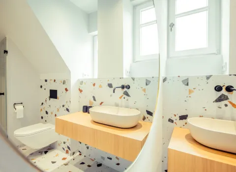 Ein großer Wandspiegel reflektiert das stilvolle Bad mit Terrazzo-Fliesen, Holzkonsole und modernem Waschbecken.