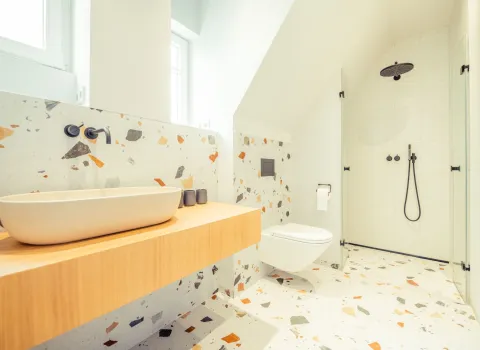 Hochwertig gestaltetes Bad mit Terrazzo-Boden, freihängendem WC und einer offenen Regendusche.