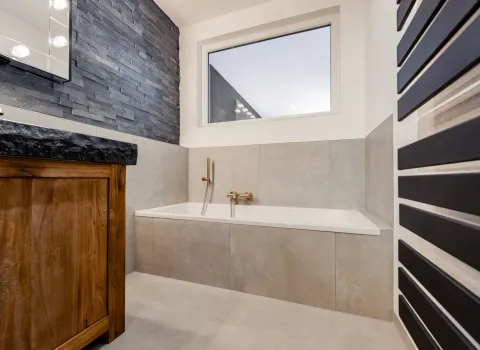 Badewanne mit heller Fliesenverkleidung und goldener Armatur in modernem Bad.