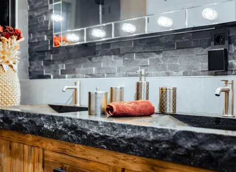 Doppelwaschbecken mit Natursteinplatte, Holzunterschrank und LED-Spiegel.