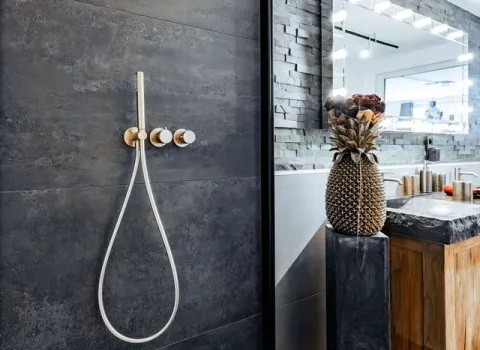 Goldene Duscharmatur an dunkler Steinwand in modernem Designbad.