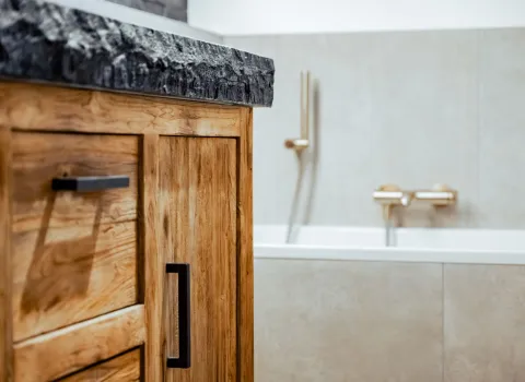 Seitenansicht eines Holzwaschtischs mit Natursteinplatte und schwarzem Griff.