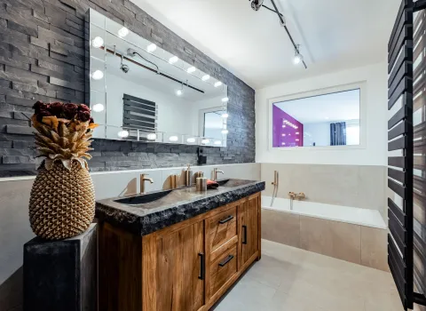 Modernes Badezimmer mit Doppelwaschtisch aus Holz, Natursteinplatte und beleuchtetem Spiegel.