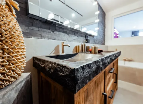 Detailansicht eines Holzwaschtischs mit massiver Natursteinplatte und Armatur in Goldoptik.
