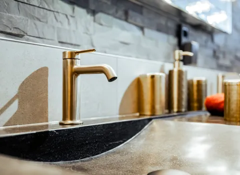 Goldene Waschtischarmatur auf Naturstein-Waschtisch mit hochwertigen Badaccessoires.