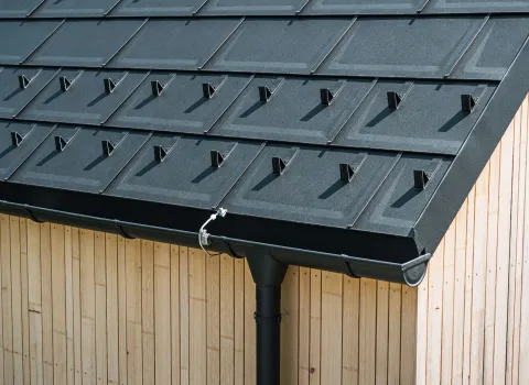 Nahaufnahme einer dunklen Alu-Dachfassade von Prefa auf hellem Holzhaus. 