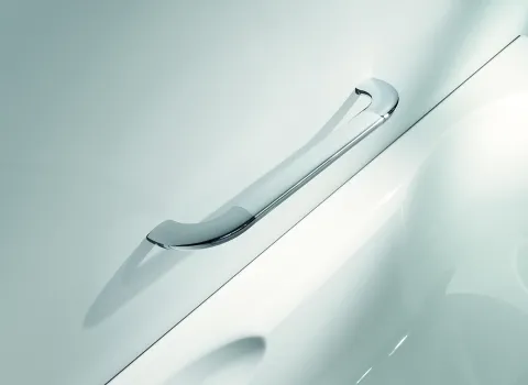 Eine silberne Haltestange ist an einer weißen Wand direkt über dem Rand einer weißen Badewanne montiert.