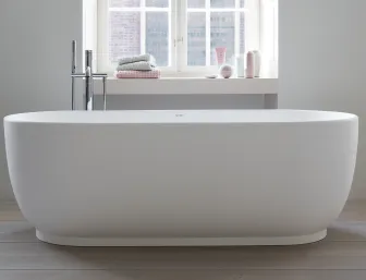 Eine freistehende, weiße Badewanne der Marke Duravit steht vor einem großen Fenster, durch das sanftes Tageslicht einfällt.