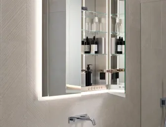 Ein moderner Badezimmerspiegelschrank mit integrierter Beleuchtung zeigt seine geöffneten Glastüren, die mehrere Regale mit Pflegeprodukten und Flaschen offenbaren. 