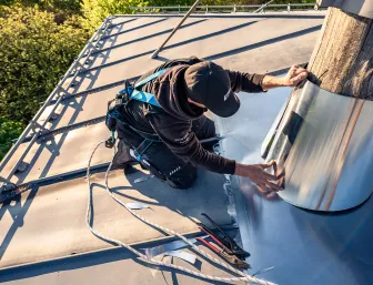 Ein Flaschner von Vitus König bringt einen runden Metallschutz ringsum des Baumstammes an.